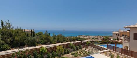 Zona de piscina con vista al mar, rodeada de vegetación y edificios.