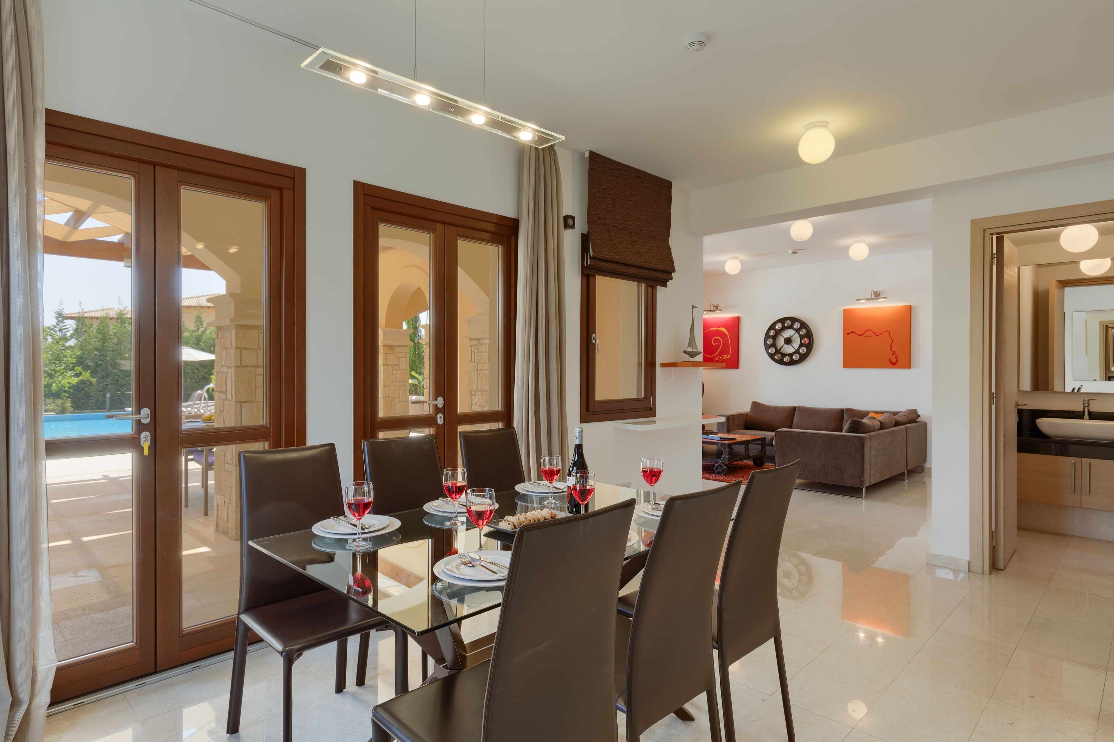 A dining area with a table set for four, a sofa in the background, and a view of the pool through glass doors.