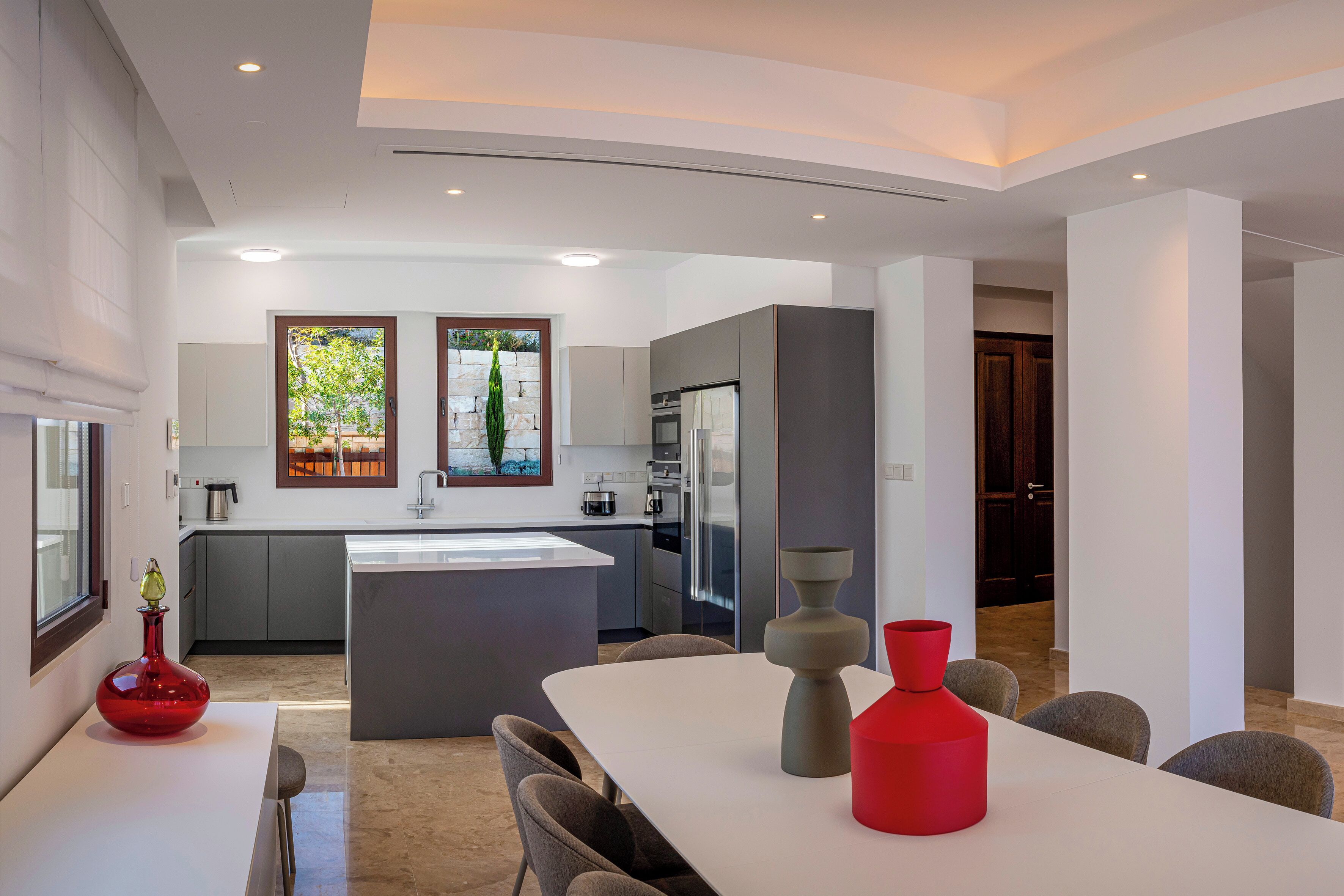 Une cuisine moderne avec un îlot central, des meubles gris et une grande fenêtre.