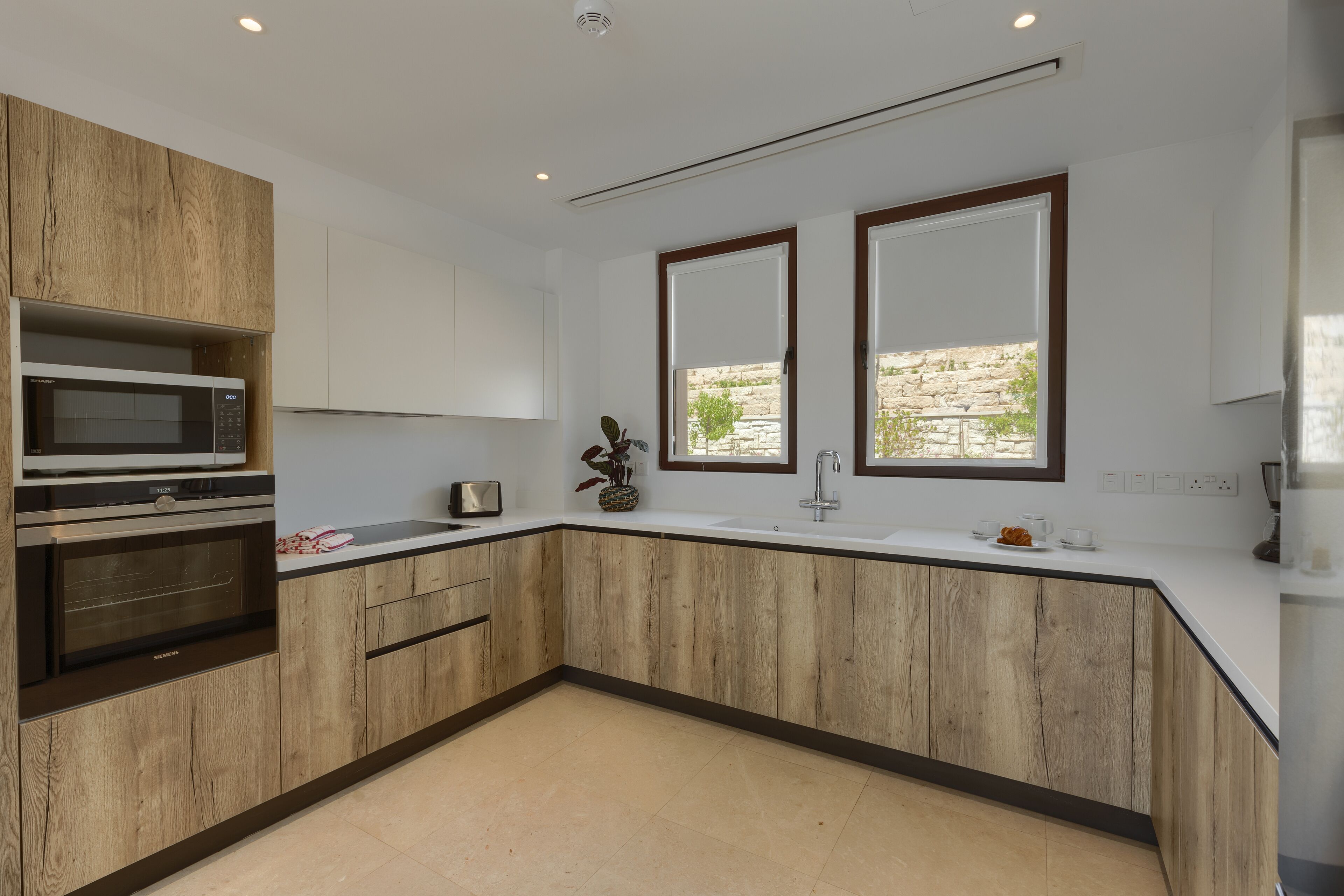 A modern kitchen with wooden cabinets, a built-in microwave, and a large window providing natural light.
