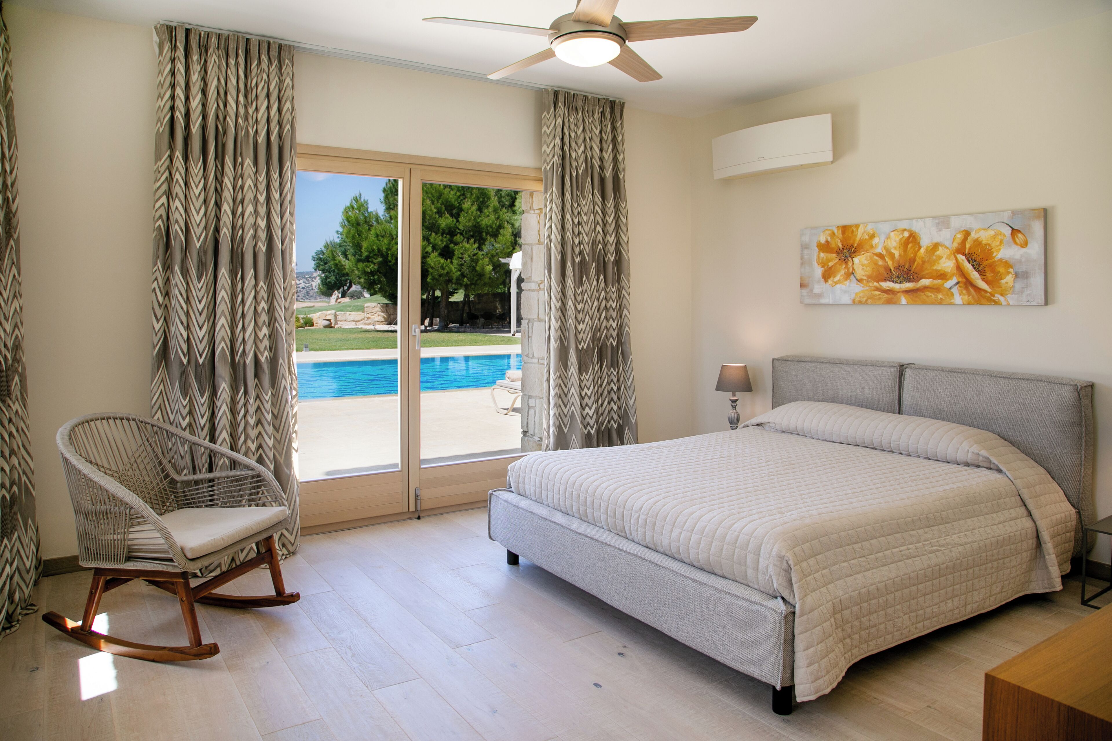A bedroom with a bed, a rocking chair, a ceiling fan, and a view of a swimming pool.