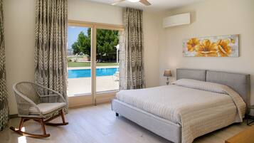 A bedroom with a bed, a rocking chair, a ceiling fan, and a view of a swimming pool.