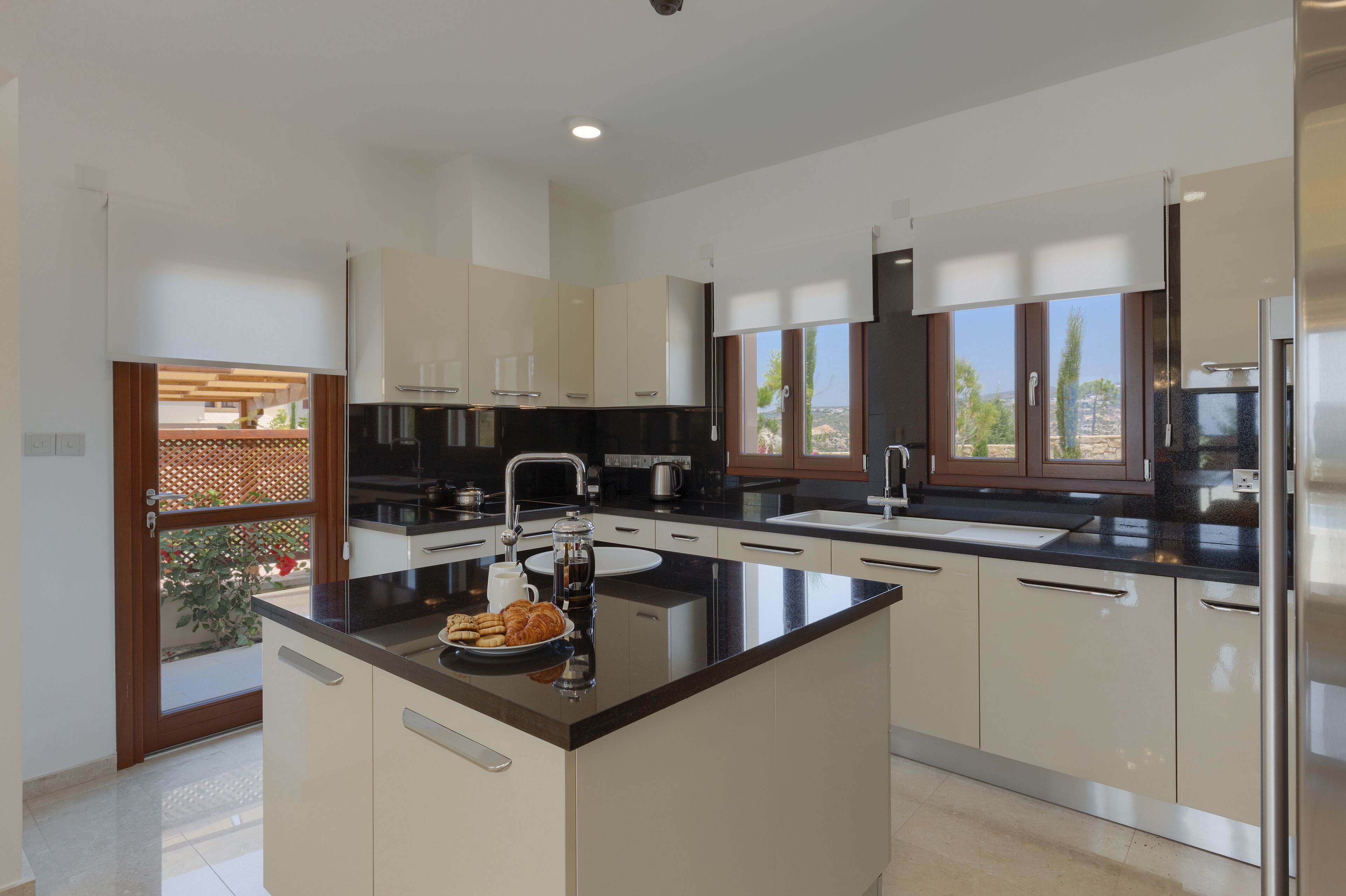 A modern kitchen with a central island, stainless steel appliances, and large windows.