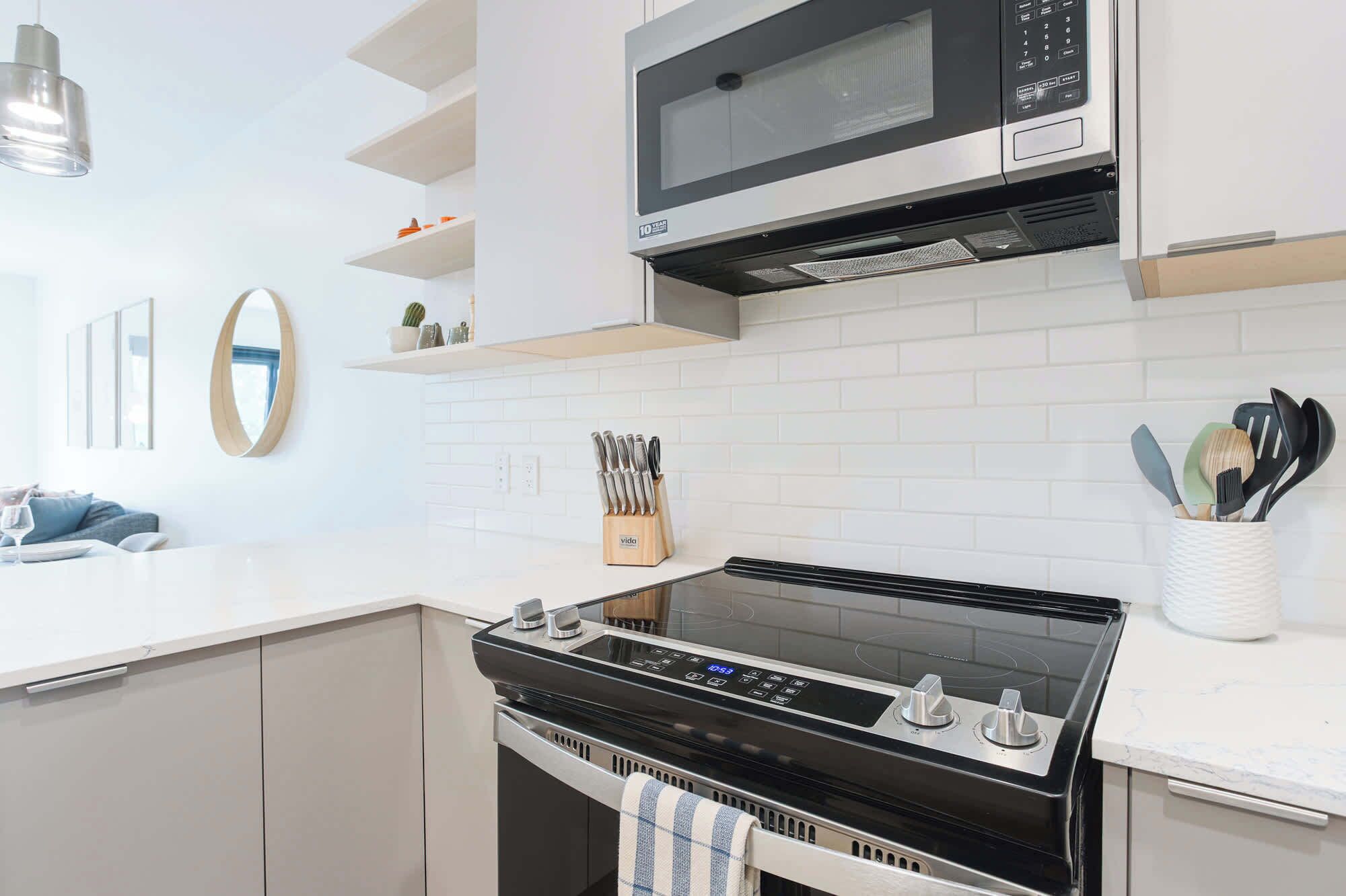 Een moderne keuken met een zwart fornuis, witte kasten, een magnetron en een messenblok.