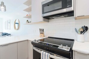 A modern kitchen with a black stove, white cabinets, a microwave, and a knife block. - Le Refuge - Revelstoke Condo with Hot Tub (Revelstoke)