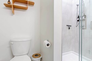 Een badkamer met een toilet, een houten bidet, een toiletrol en een douchecabine van glas.