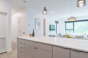 A modern kitchen with a large island, pendant lights, and a window with a view of greenery.