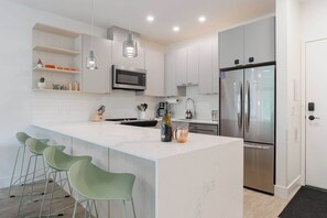 A modern kitchen with a central island, stainless steel appliances, and green bar stools.