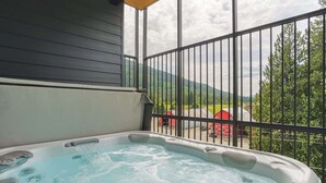 A hot tub on a balcony with a view of a red barn and green hills. - Le Refuge - Revelstoke Condo with Hot Tub (Revelstoke)