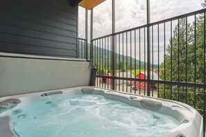 A hot tub on a balcony with a view of a red barn and green hills.