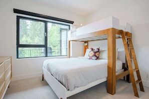 Un lit superposé avec une échelle, une fenêtre donnant sur les arbres et une commode.