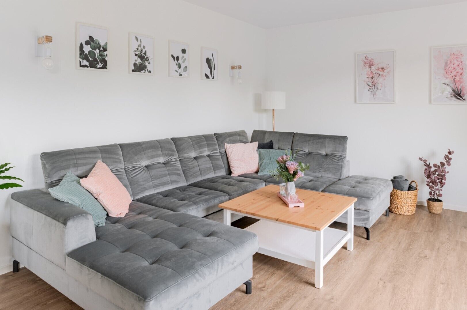 A modern living room with a grey sectional sofa, a wooden coffee table, and a vase of flowers.