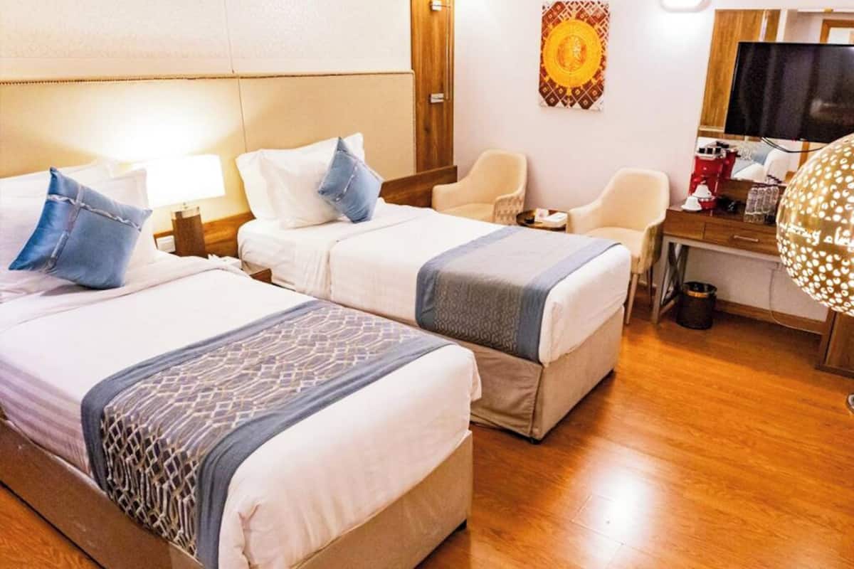 A hotel room with two beds, a desk, a chair, and a television.