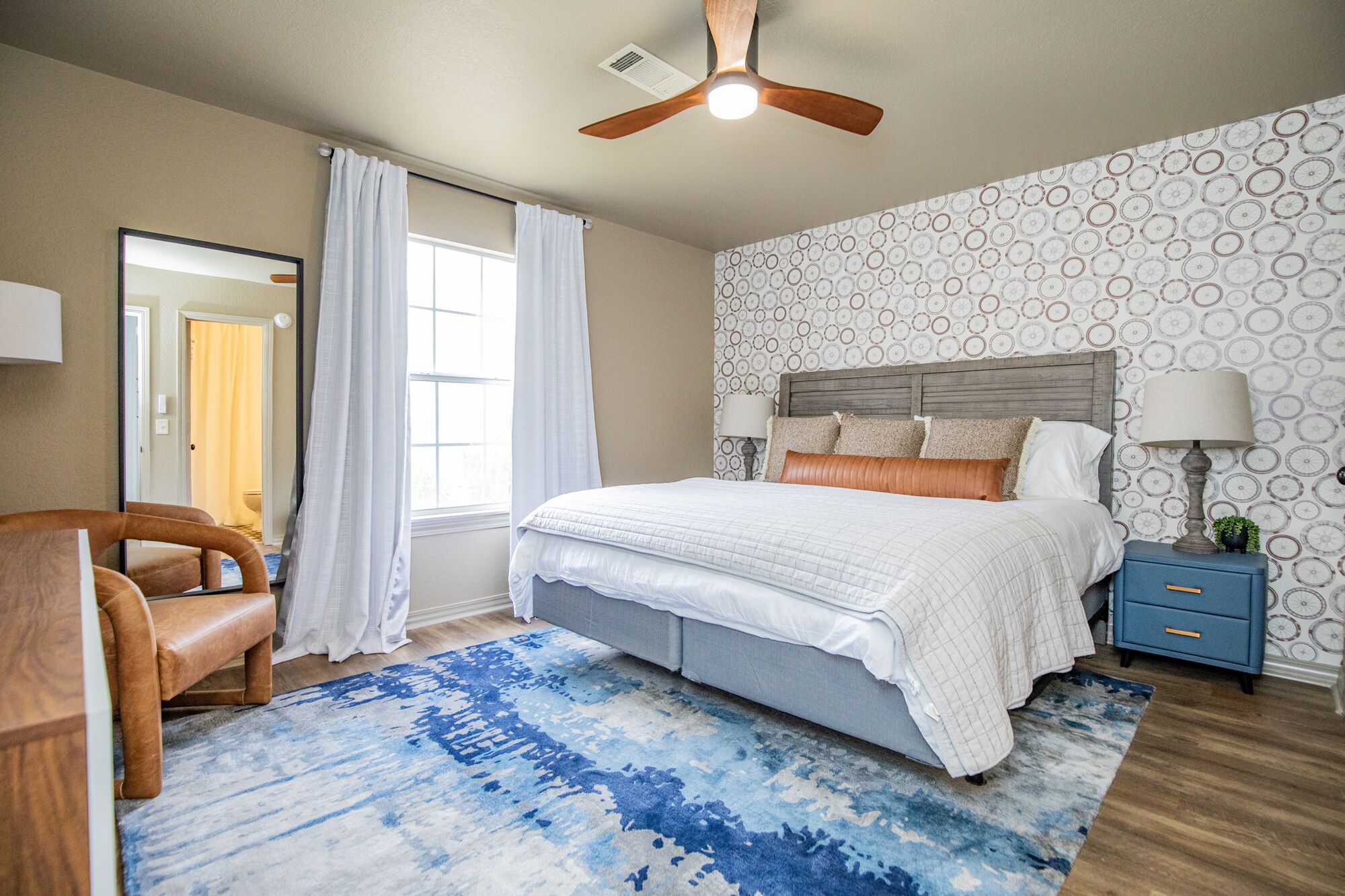 A bedroom with a bed, a nightstand, a chair, a ceiling fan, and a window with curtains.