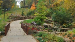 A pathway leading through a garden with a stone wall and a wooden bridge. - Downtown Trailside Cottage (Bentonville)