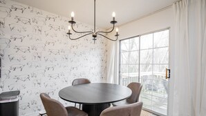 A dining area with a round table, four chairs, a chandelier, and a wall with pig illustrations. - Downtown Trailside Cottage (Bentonville)