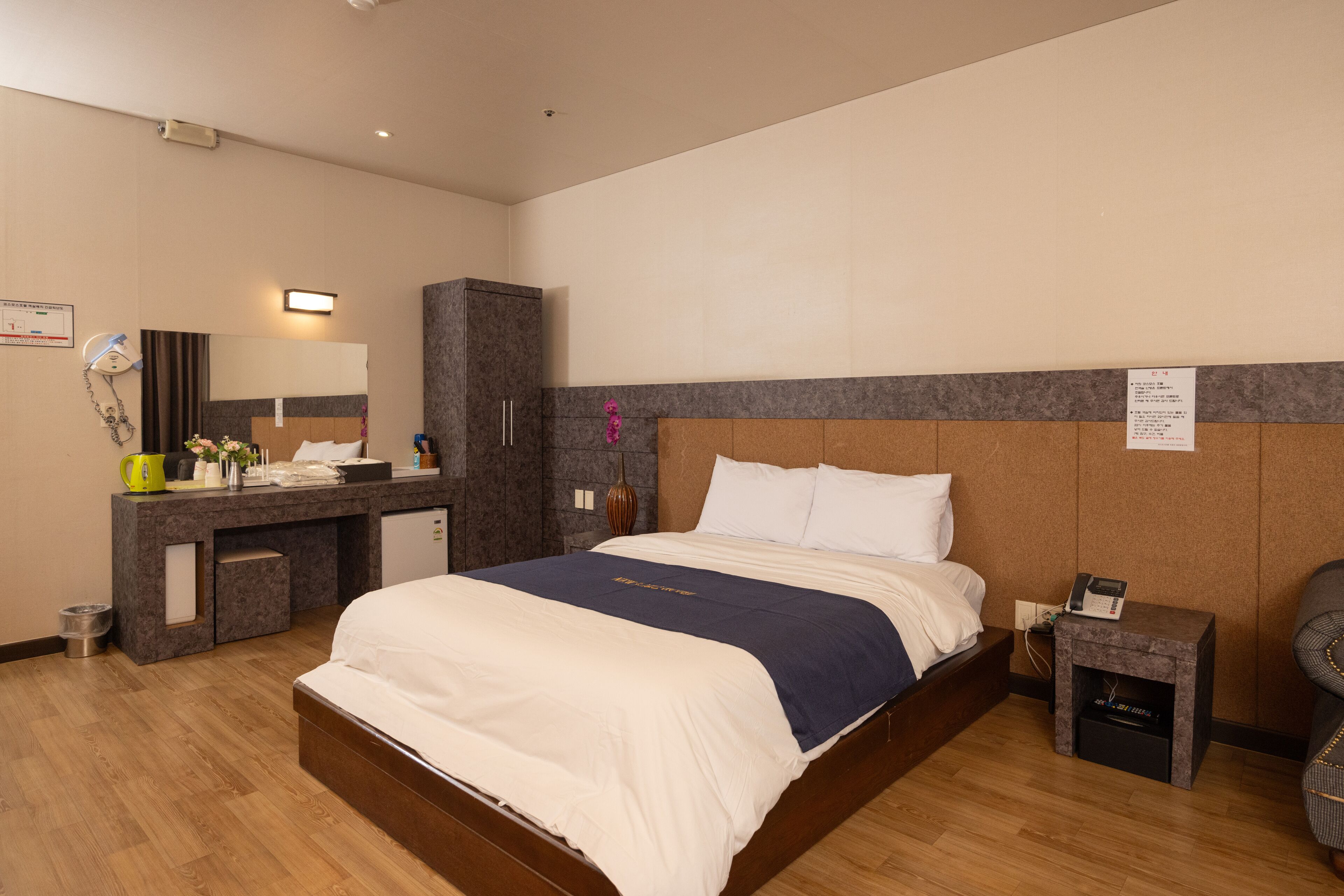 A hotel room with a bed, a desk, a mirror, a small cabinet, and a nightstand with a phone.