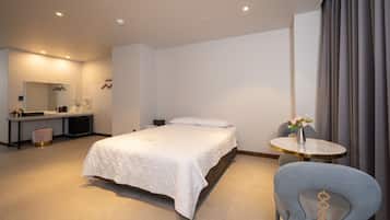 A modern hotel room with a large bed, a desk with a mirror, a chair, and a small table with a vase of flowers.
