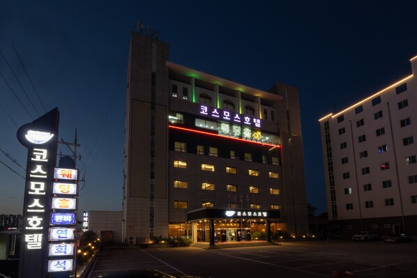 Un hotel de varios pisos con señalización iluminada y un estacionamiento.