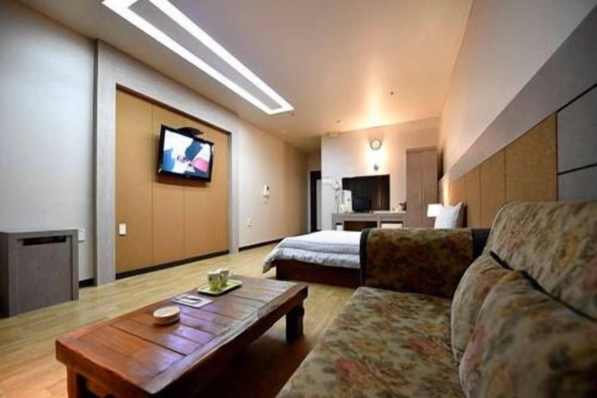 A hotel room with a bed, a sofa, a television, and a wooden coffee table.