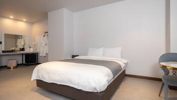 A modern hotel room with a large bed, a vanity with a mirror, and a chair.