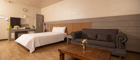 A hotel room with a bed, a sofa, a coffee table, a desk, and a mirror.