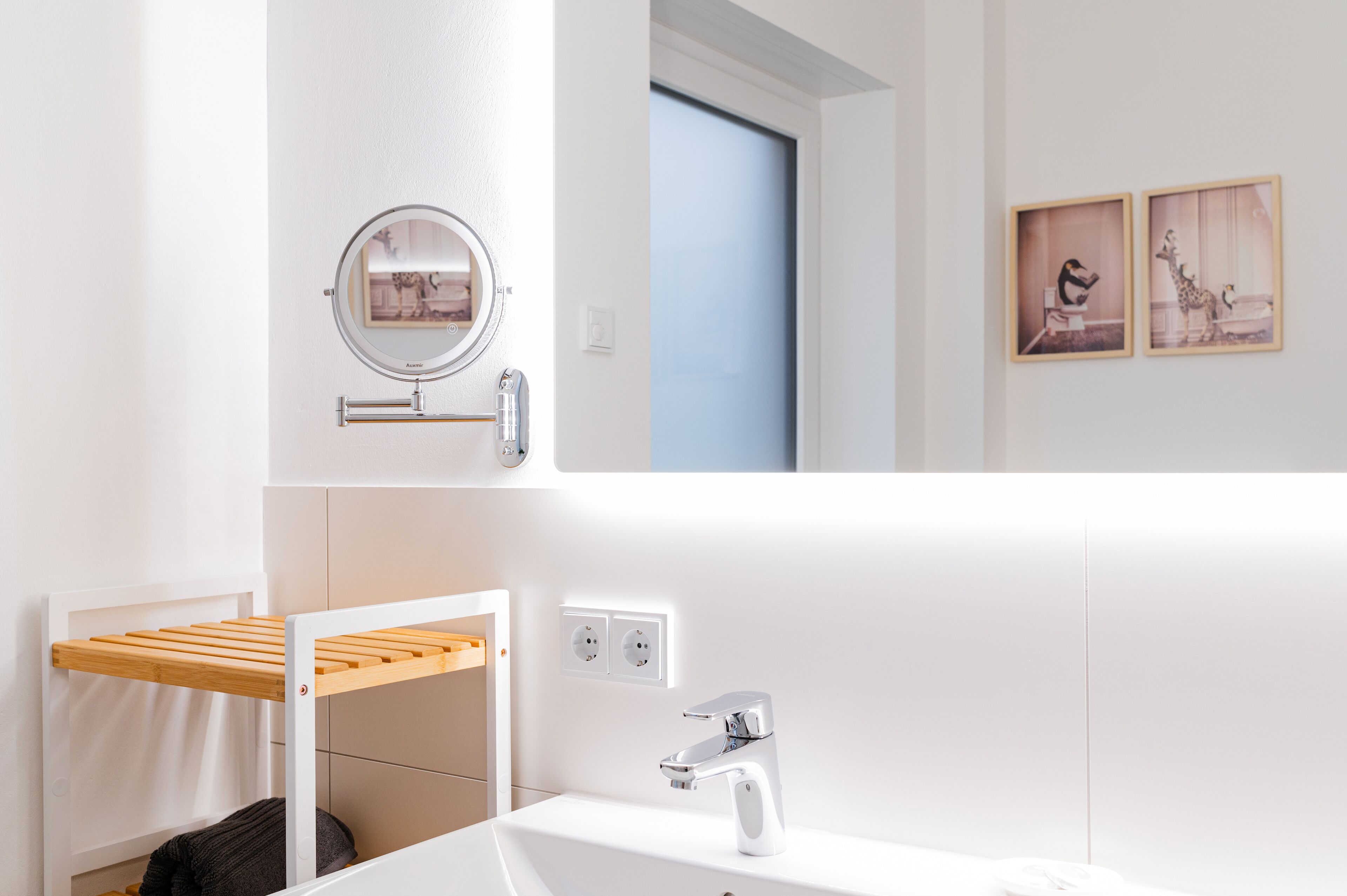 Une salle de bain moderne avec un lavabo blanc, un miroir, un porte-serviettes et deux prises électriques murales.