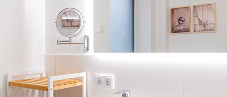 Une salle de bain moderne avec un lavabo blanc, un miroir, un porte-serviettes et deux prises électriques murales.