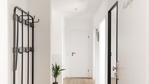 A hallway with a black metal rack, a potted plant, and a white door at the end. - Ferienwohnung Heideloft (Faßberg)