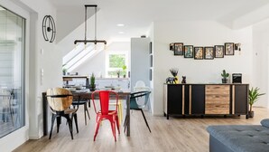 A modern kitchen with a dining area, featuring a wooden dining table, chairs, and a black and wood-colored cabinet. - Ferienwohnung Heideloft (Faßberg)