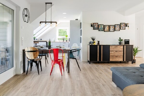 A modern kitchen with a dining area, featuring a wooden dining table, chairs, and a black and wood-colored cabinet.