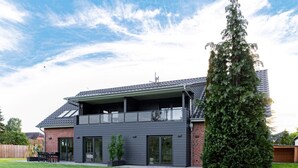 A modern two-story house with a balcony, a large tree in the yard, and a well-maintained lawn. - Ferienwohnung Heideloft (Faßberg)