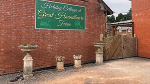 Un bâtiment en briques sur lequel est apposée une enseigne indiquant : « Location de cottages de vacances à la ferme de Great Houndbeare ».