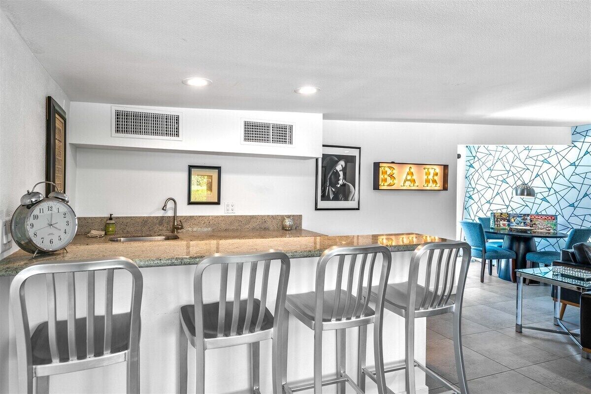 A modern kitchen with a bar area, featuring a sink, a clock, and framed artwork on the walls.