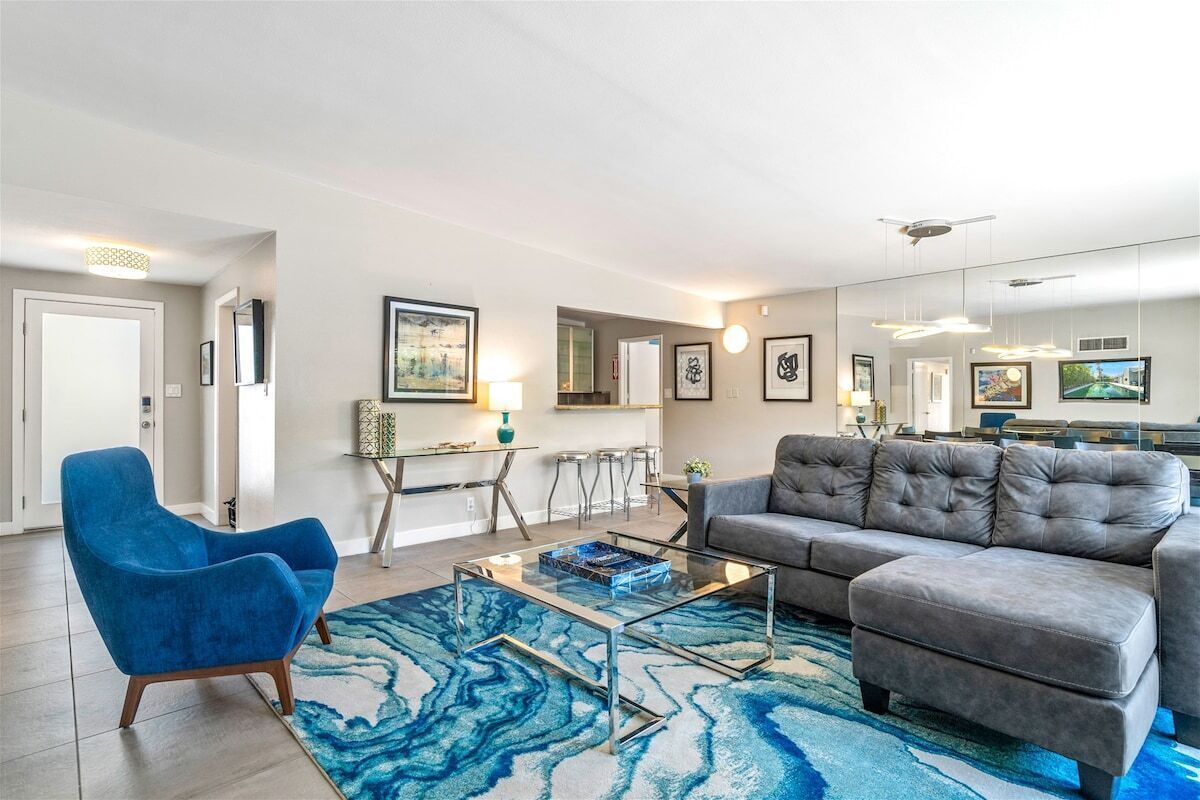 Una sala de estar moderna con un sillón azul, un sofá gris, una mesa de centro de vidrio y un tapete azul estampado.