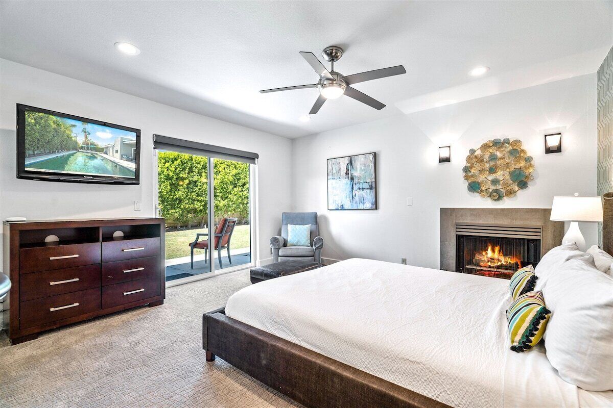 A bedroom with a bed, a television, a fireplace, and a ceiling fan.