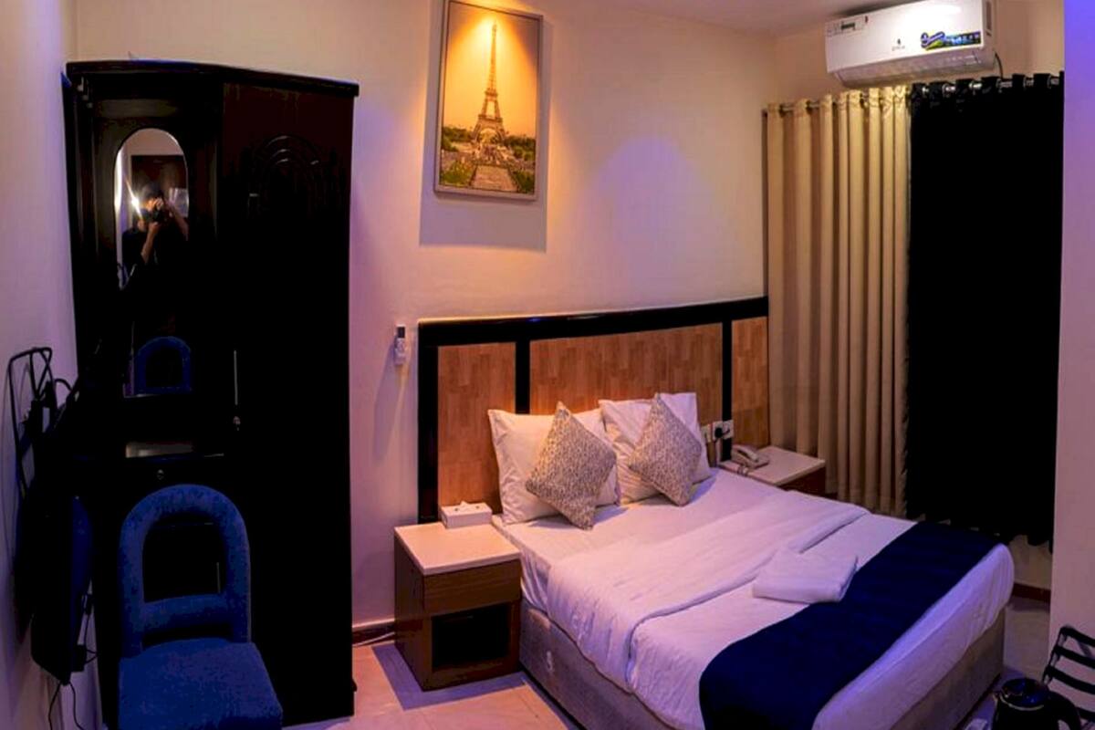 Hotelkamer met een bed, een bureau, een stoel, een airconditioner en een foto van de Eiffeltoren.