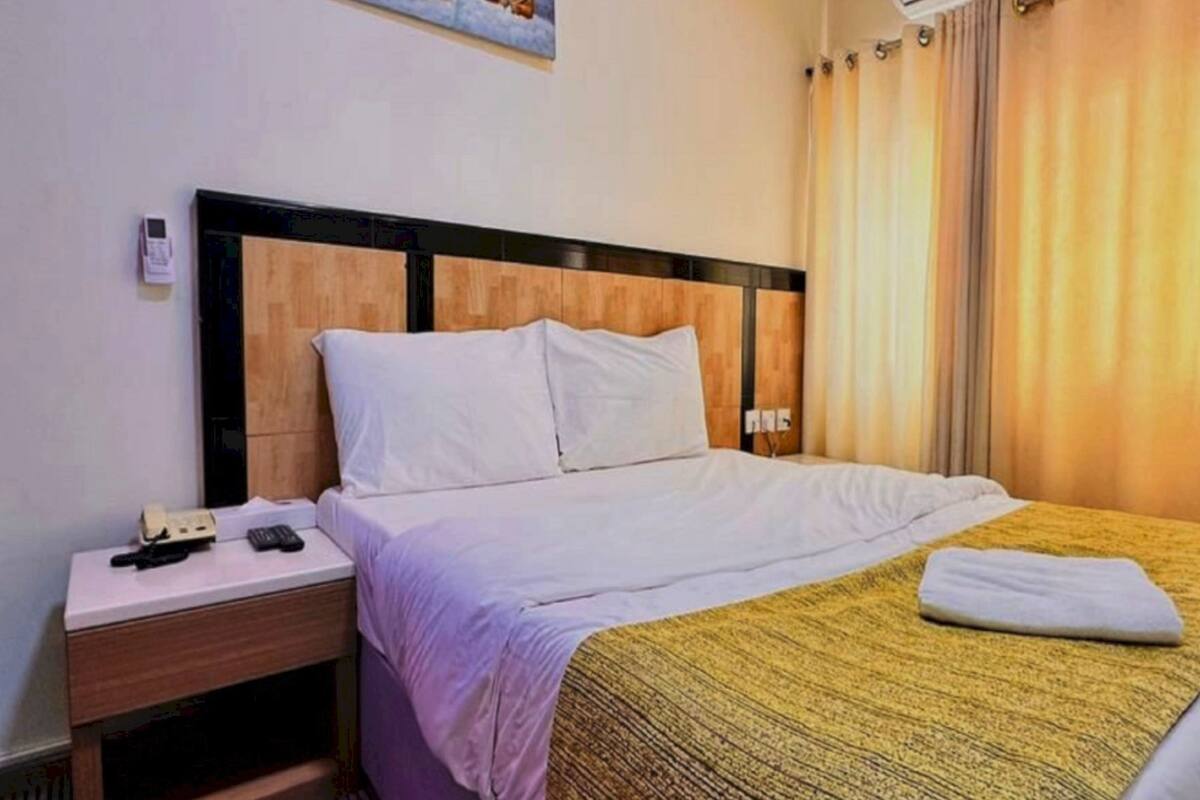 Een hotelkamer met een bed, nachtkastje, telefoon en raam met gordijnen.