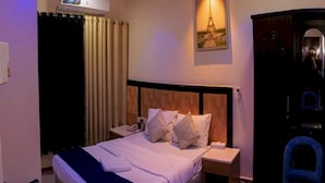 Une chambre d’hôtel comprenant un lit, une table de chevet, une chaise, une armoire et un tableau représentant la Tour Eiffel.