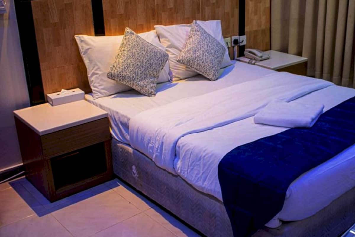 Een net opgemaakt bed met witte lakens en twee kussens met een patroon, een nachtkastje met een telefoon en een bijzettafeltje met een lamp.