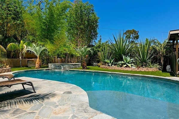 A swimming pool with stone tiles, surrounded by tropical plants and a waterfall feature.