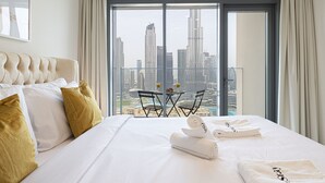 A hotel room with a large bed, a view of a cityscape, and a balcony with a table and chairs.