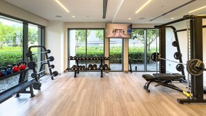 A modern gym with weightlifting equipment, benches, and a TV screen.