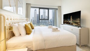 Une chambre d’hôtel moderne dotée d’un grand lit, offrant une vue sur la ville, d’un téléviseur à écran plat et d’un design minimaliste.