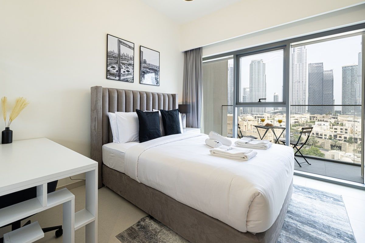 Une chambre d’hôtel moderne dotée d’un grand lit, d’un bureau et d’un balcon offrant une vue sur la ville.