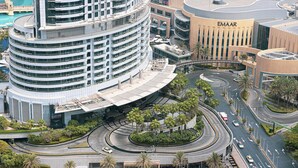 A modern, multi-story building with a curved facade, a prominent EMAAR sign, and a complex road layout with palm trees and greenery.