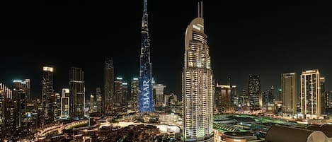 A nighttime cityscape with prominent skyscrapers, including a tall, illuminated tower and a curved building with 'EMAR' signage.