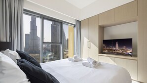 A hotel room with a large bed, a TV mounted on the wall, and a view of city skyscrapers through the window.