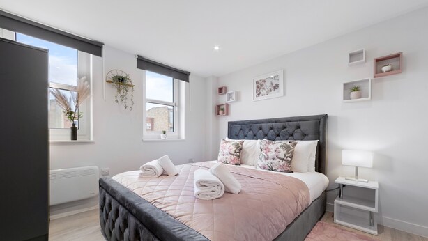 Une chambre moderne avec un grand lit, une table de chevet avec une lampe et une fenêtre donnant sur des immeubles.