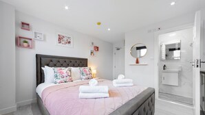 Une chambre moderne avec un grand lit, des tables de chevet, un miroir et une salle de bain équipée d’une douche et d’un lavabo.